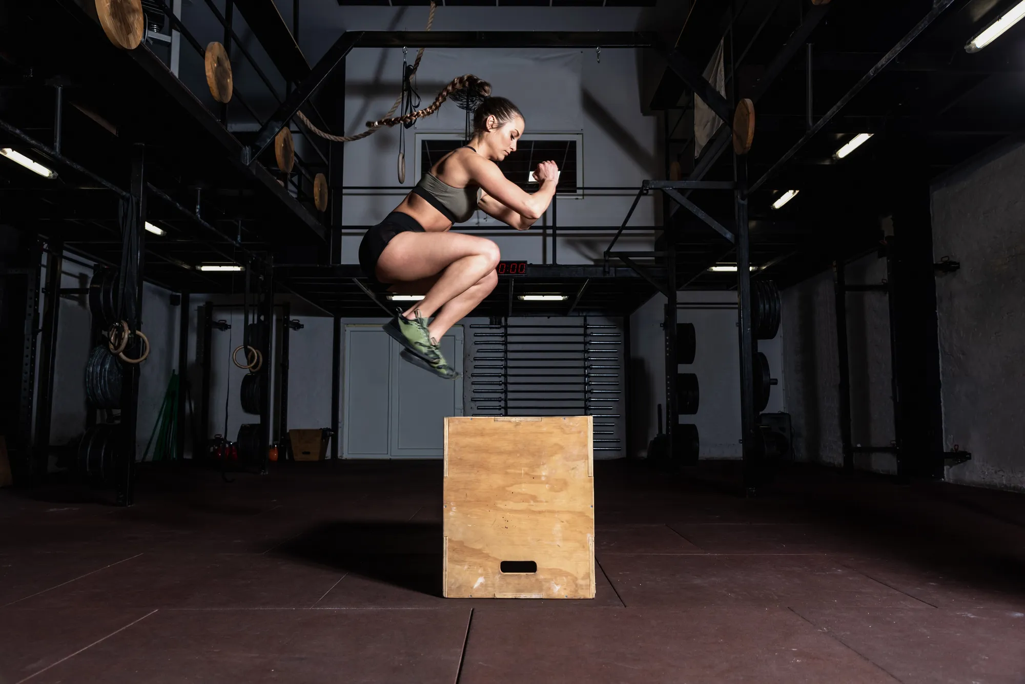 Sportive en plein saut au-dessus d’une box en bois dans une salle équipée.